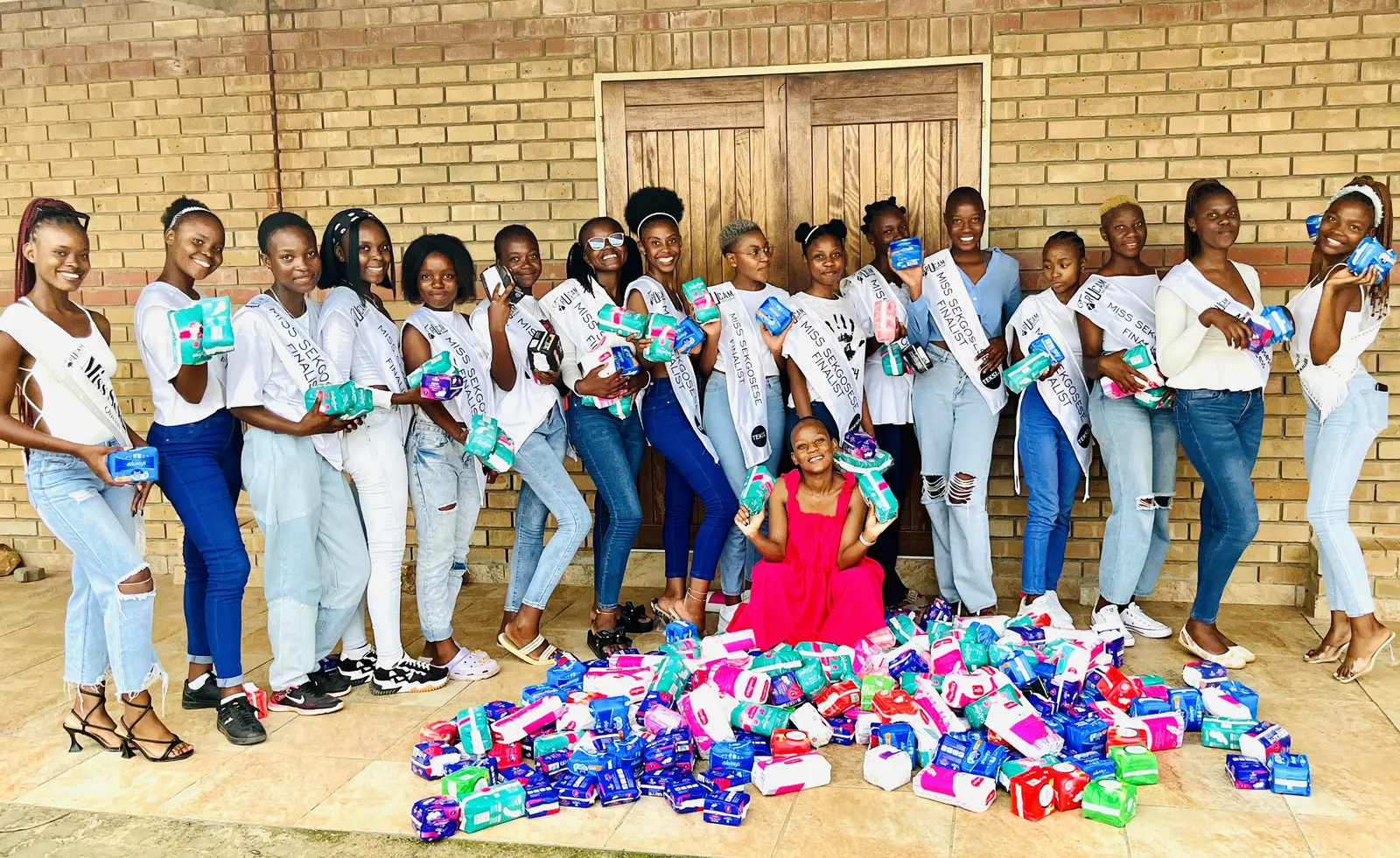 Pageant contestants with a large pile of donated sanitary towels